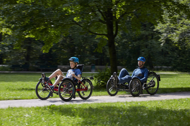 A teen and a man are riding on Gekko recumbent bike on a path - Un adolescent et un homme font du vélo allongé Gekko sur un chemin