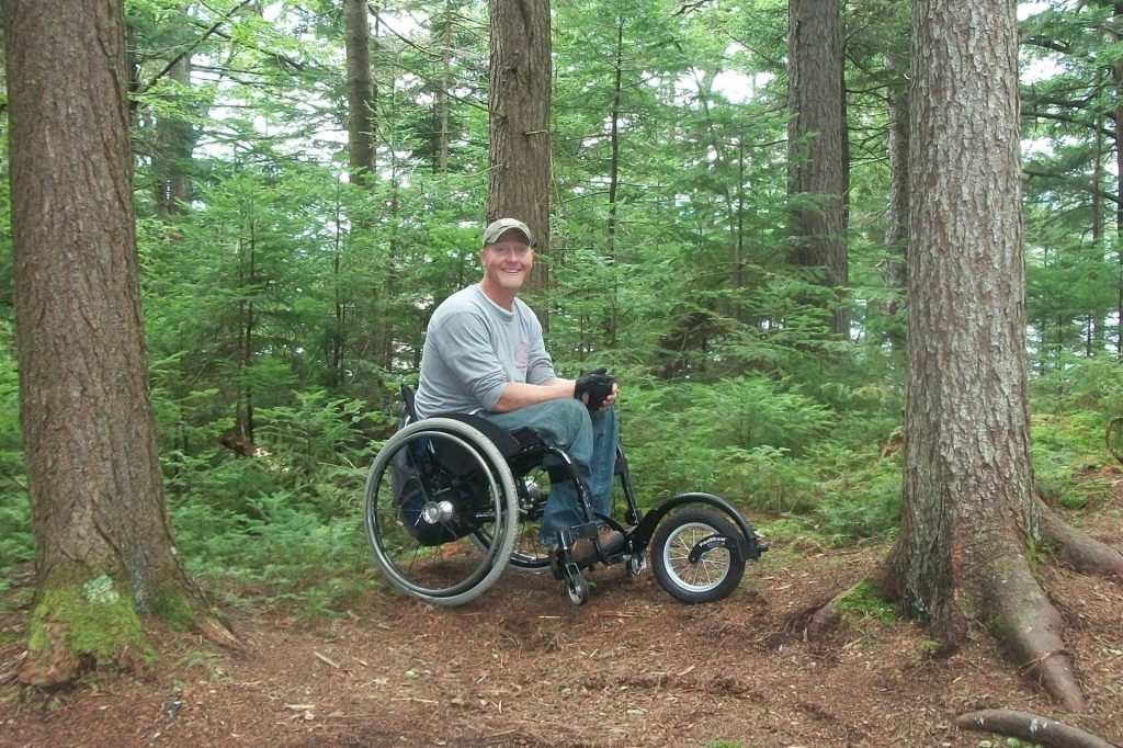 Français: un homme est en fauteuil roulant avec un FreeWheel au milieu des bois English: a man in a wheelchair with a FreeWheel in the middle of the woods