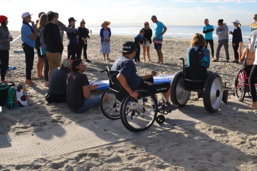 Groupe de personnes en fauteuil roulant et pas en fauteuil sur un tapis de plage, sur la plage