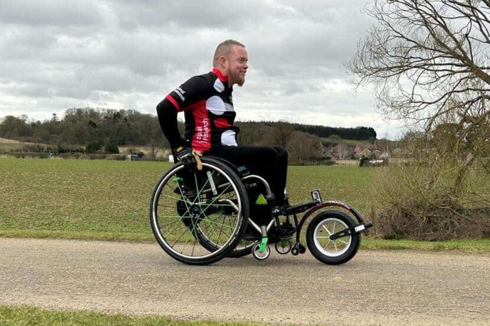 Un homme en tenue de sport et sur un fauteuil roulant avec un Track Wheel est en train d'avancer sur une route, avec le sourire