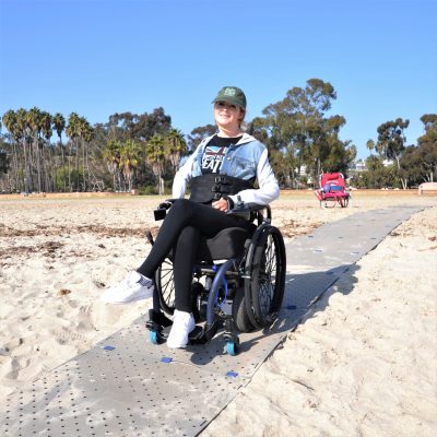 Une femme est dans un fauteuil roulant, sur un Access Trax, sur du sable