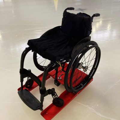 Un fauteuil roulant sur un Lugicap Ice Perf rouge sur la glace d'une patinoire / A wheelchair on a red Lugicap Ice Perf on the ice of a rink